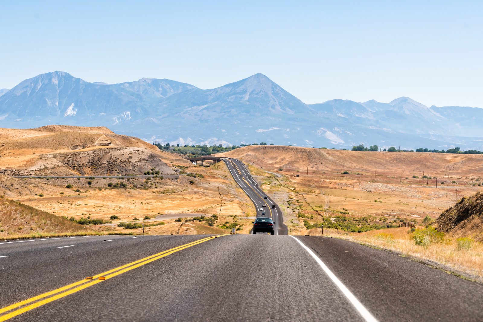 An open Colorado highway stretching toward distant mesas under a wide sky