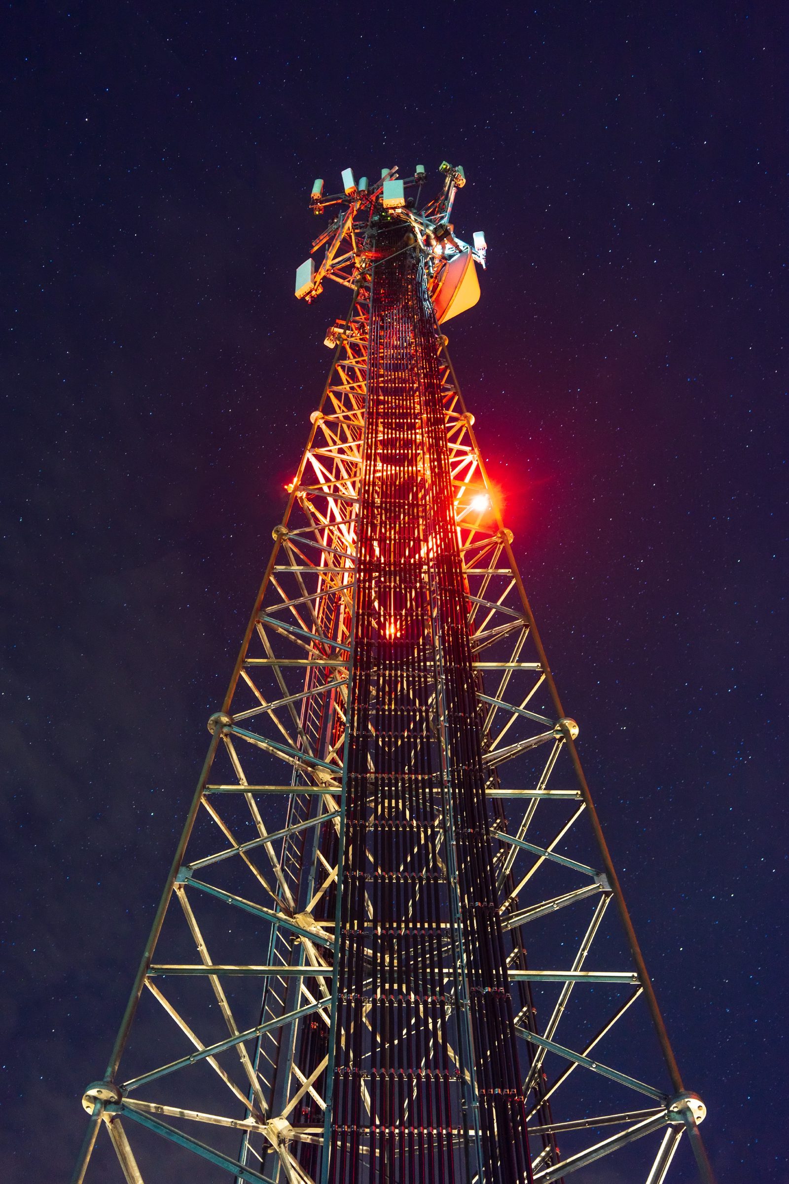 A lit cellular tower rising into a starry night sky